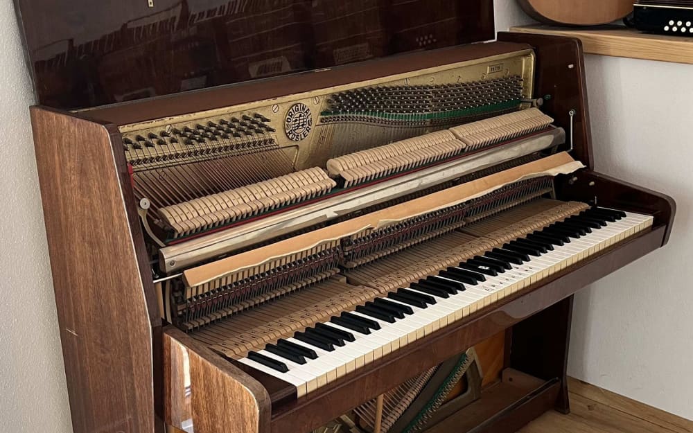 Pianino Gustav Rösler 103 zboku v domácím prostředí s dalšími hudebními nástroji na zdi
