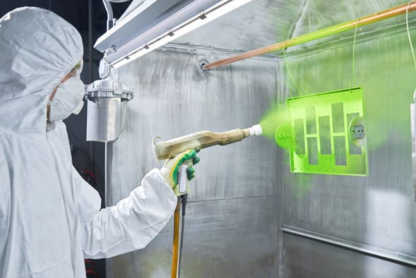 Worker-in-a-protective-suit-sprays-bright-green-powder-coating-material-from-a-spray-gun-onto-a-rectangular-metal-part