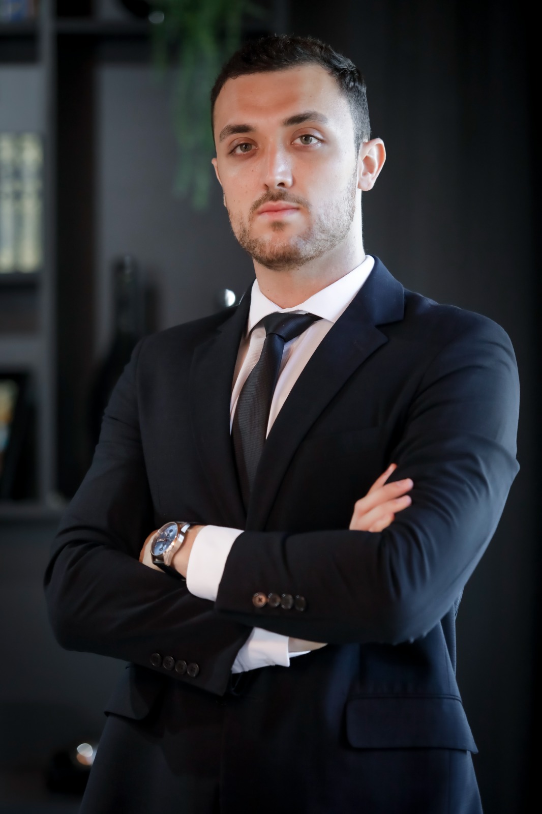 Retrato profissional do Dr. Ramon Moreto, advogado usando terno escuro e óculos em escritório moderno, demonstrando confiança e profissionalismo