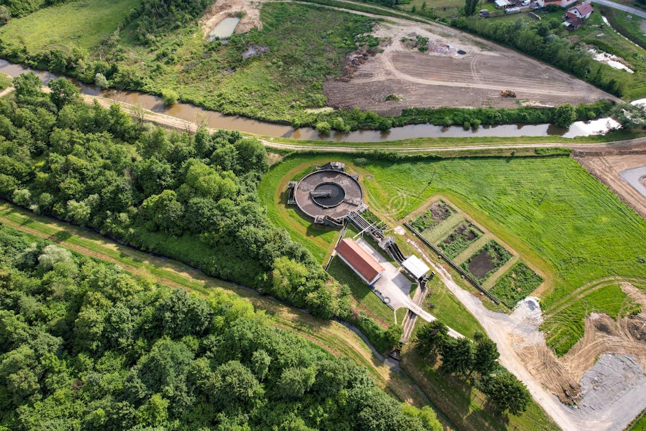 An aerial view (4:3) of a modern wastewater treatment plant integrated into a green urban environment, showing the various stages of the E-MLE-OSA process with clear, treated water flowing out into a clean river. Emphasize advanced technology and environmental harmony. - Photo by Vladimir Srajber on Pexels