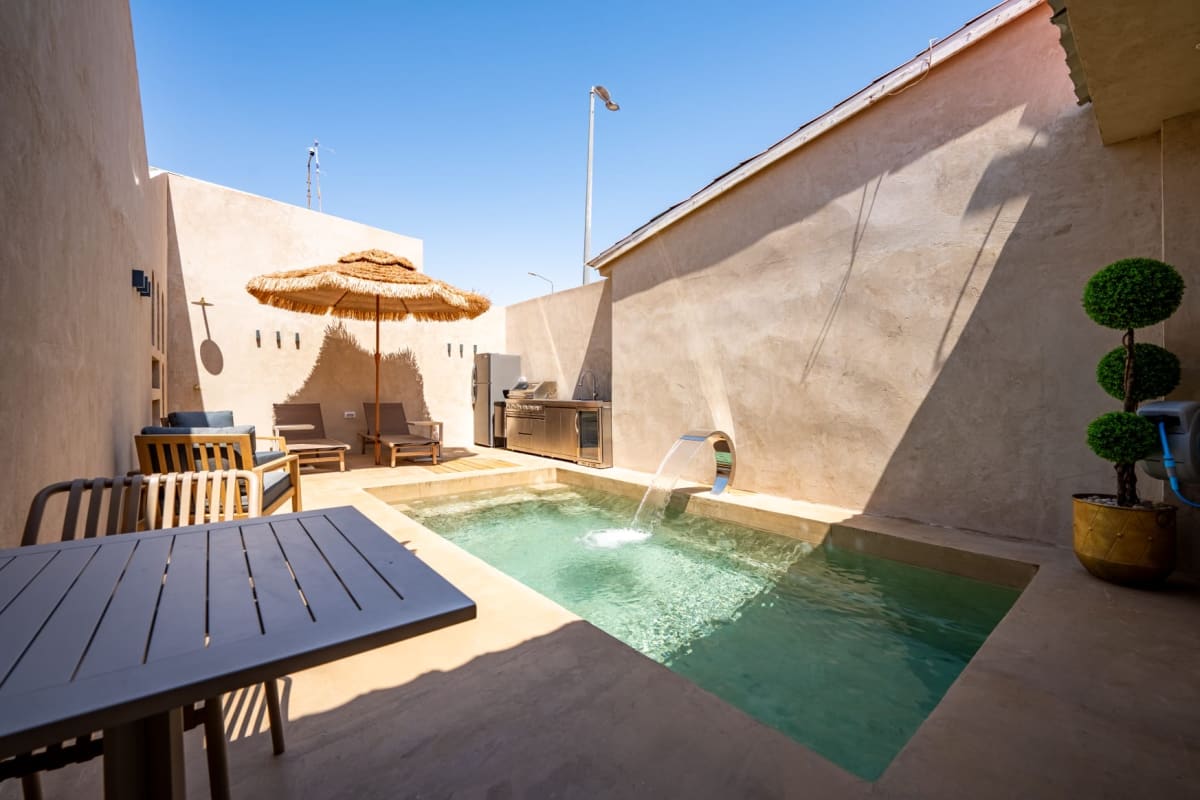 Small private pool with a waterfall in an inner courtyard of a villa in central Eilat, with a straw umbrella, sun loungers, and an outdoor kitchen