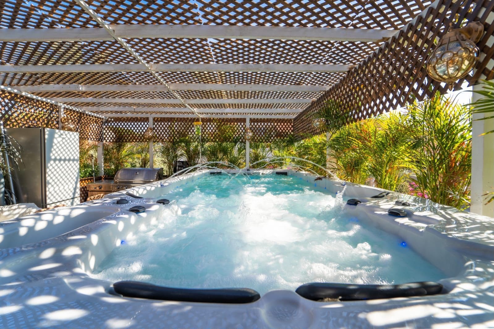 Spa pool with jets under a wooden pergola, surrounded by greenery, in the courtyard of a holiday complex in Eilat