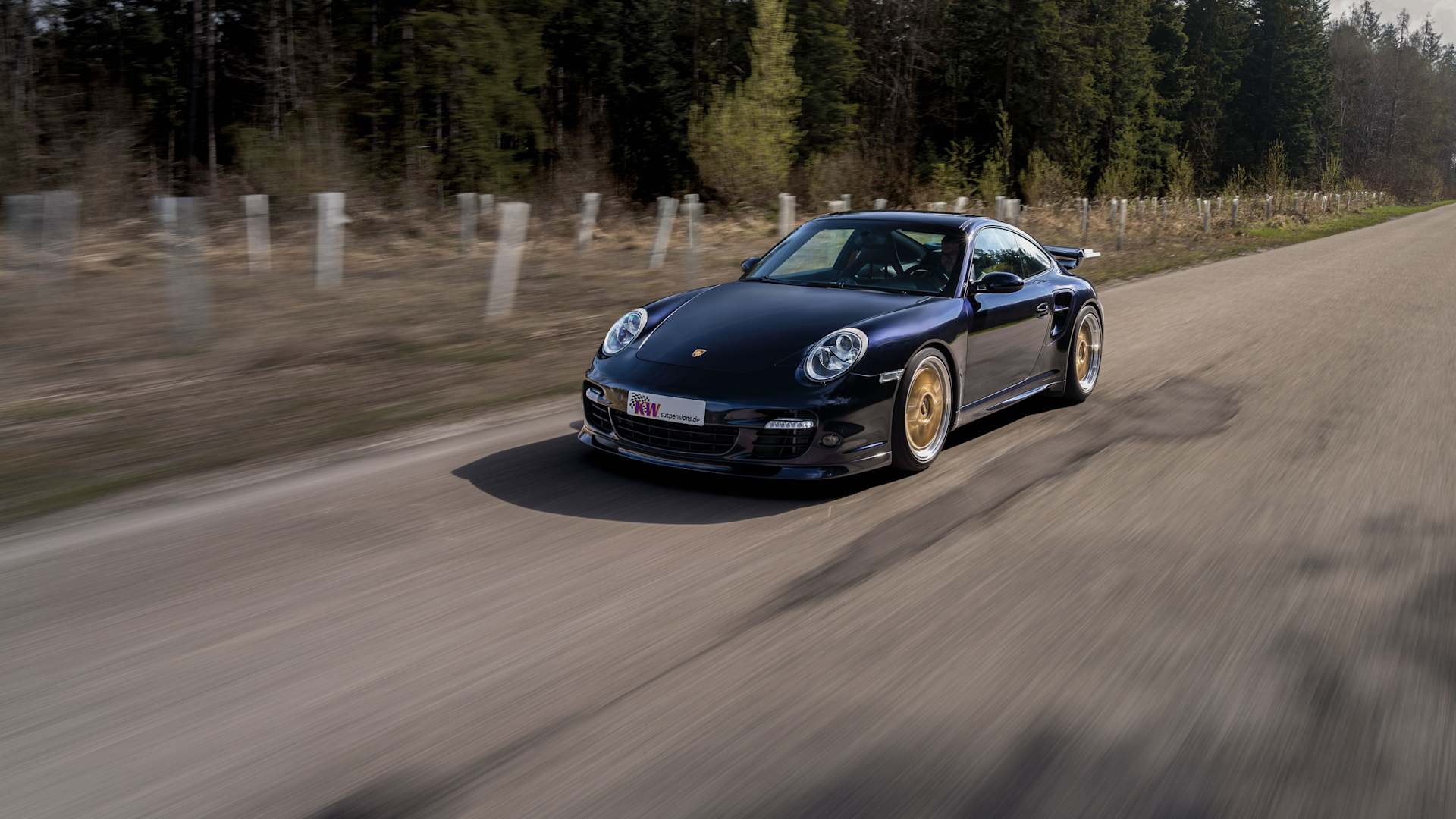 Black Porsche 997 with coilovers by KW suspensions driving on a country road