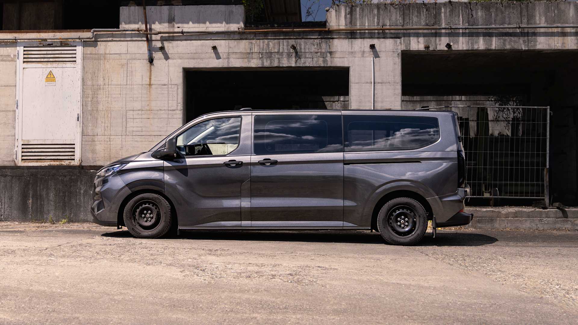 Side view of a dark gray Ford Transit Custom with KW coilover suspension in front of an old industrial building