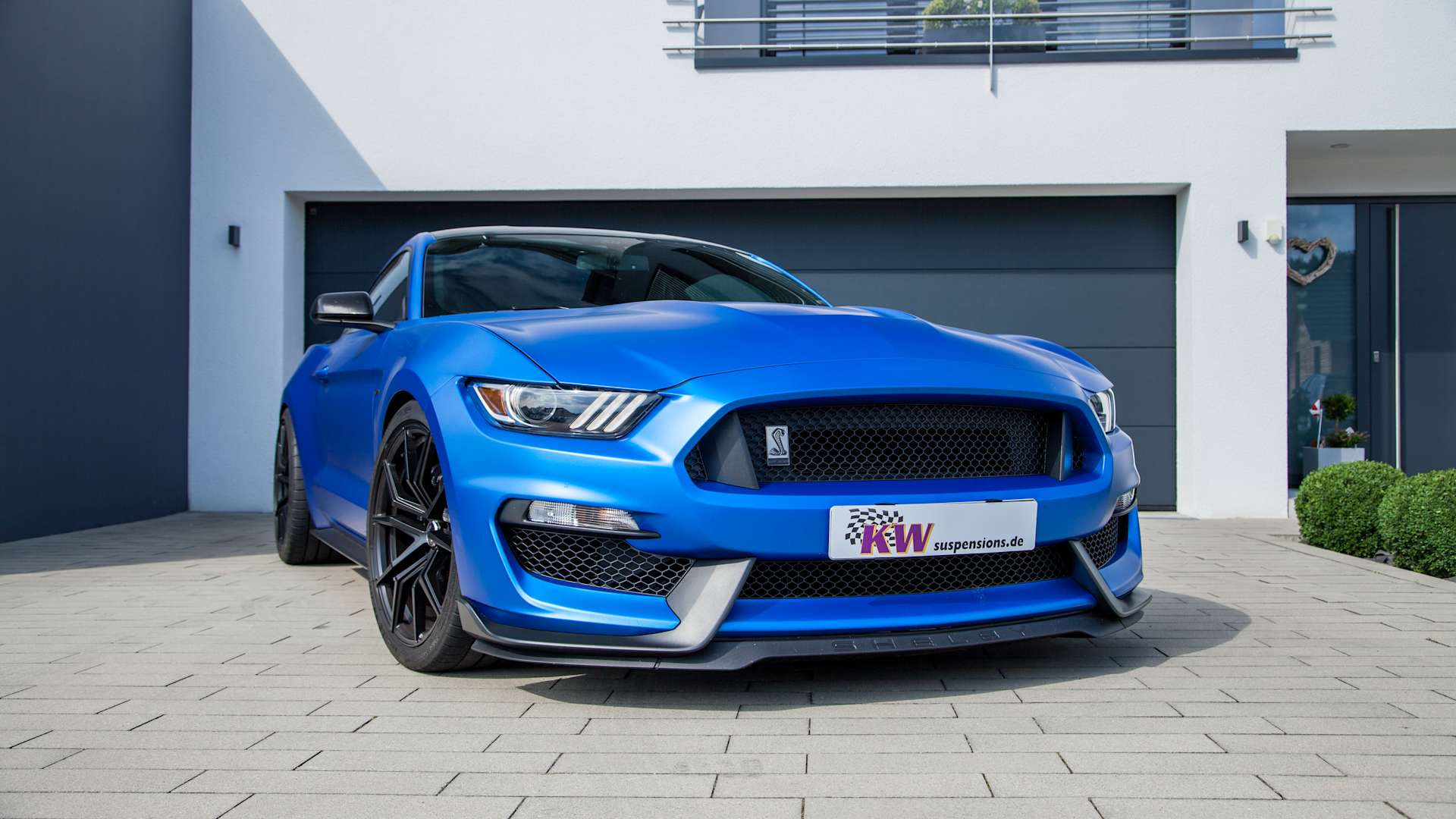 Standbild eines blauen Ford Mustang mit KW Gewindefahrwerk vor einer Garageneinfahrt