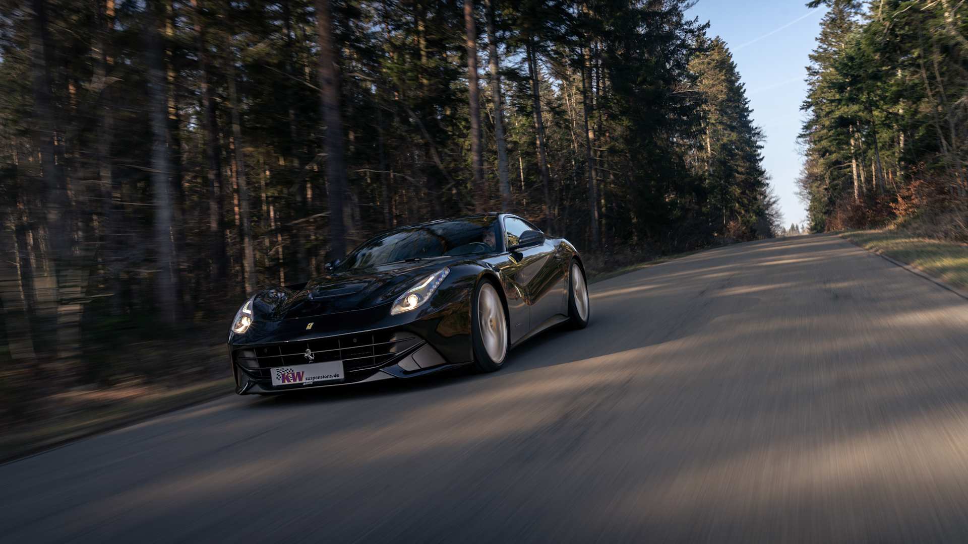 A Ferrari F12 driving dynamically with continuous height adjustment on a country road through the woods