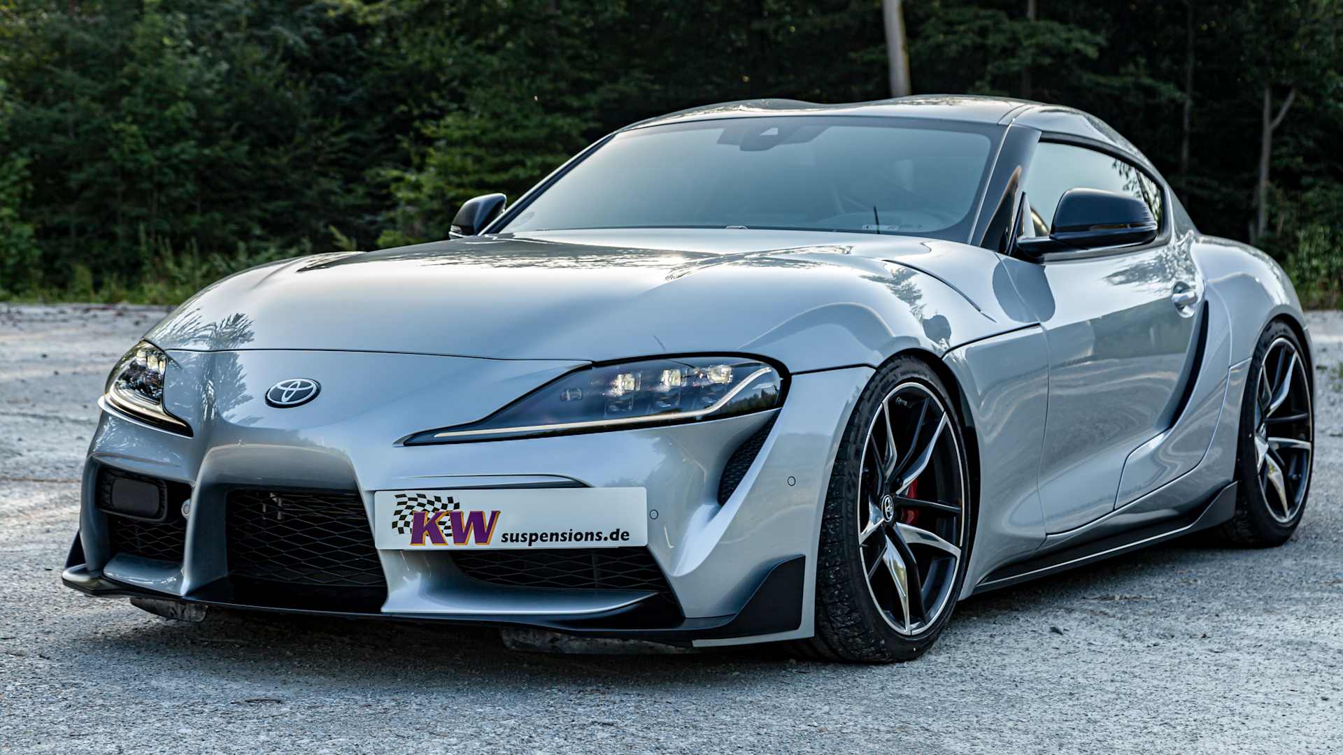 A lowered Toyota GR Supra with KW coilover suspension in an asphalt parking lot in the woods