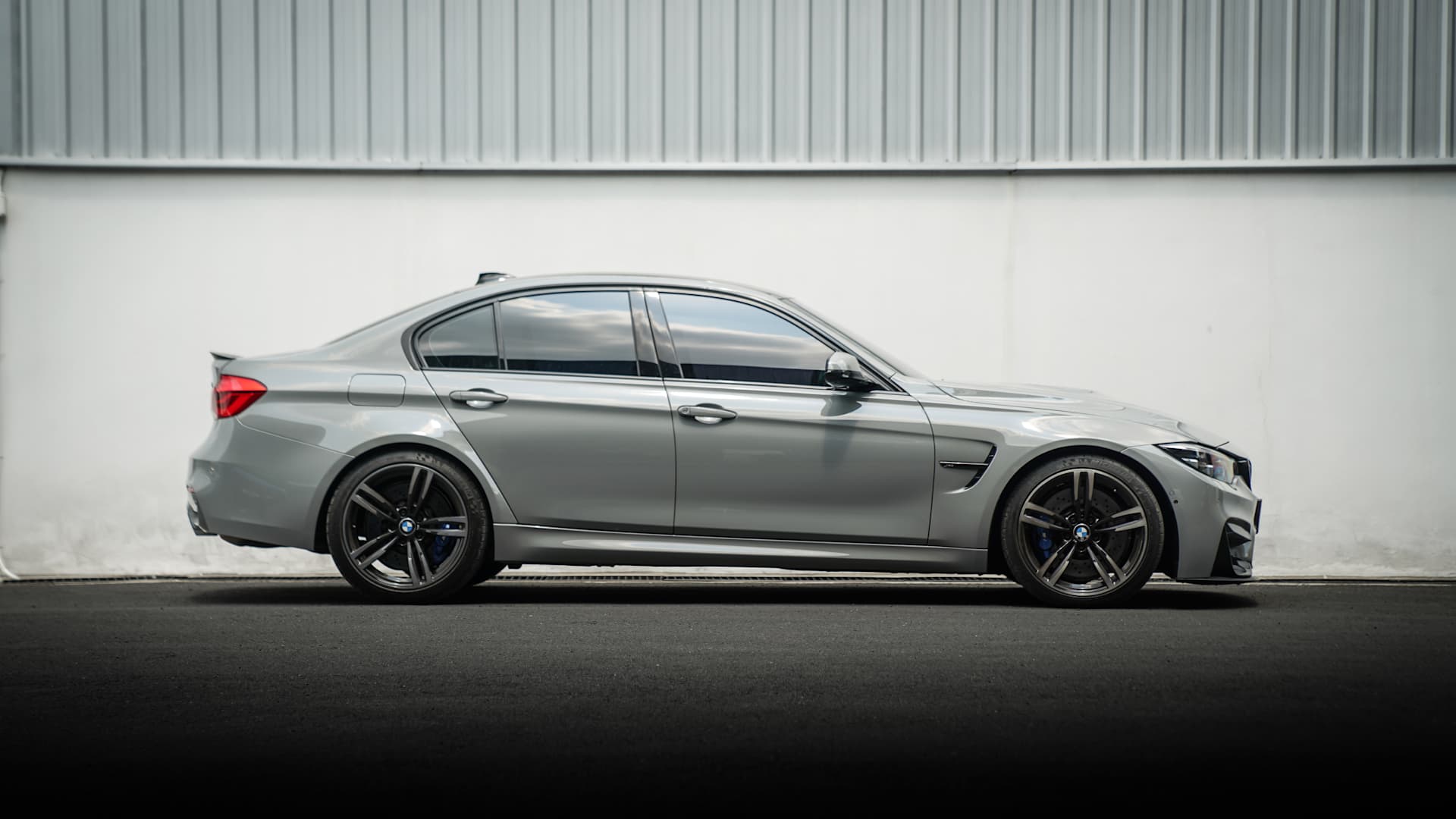 BMW M3 (F80) lowered with KW coilover suspension - side view in front of an industrial building