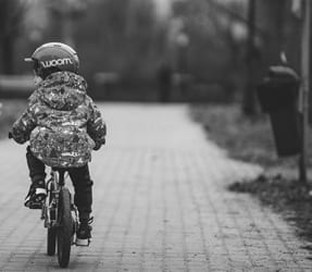Billede af et barn bagfra, der cykler med cykelhjelm
