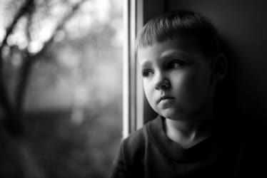 en lille dreng kigger fraværende ud af vinduet med en trist mine