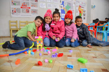 Fem børn sidder storsmilende bag deres farverig LEGO tårn i et af Red Barnets børnevenlige områder.