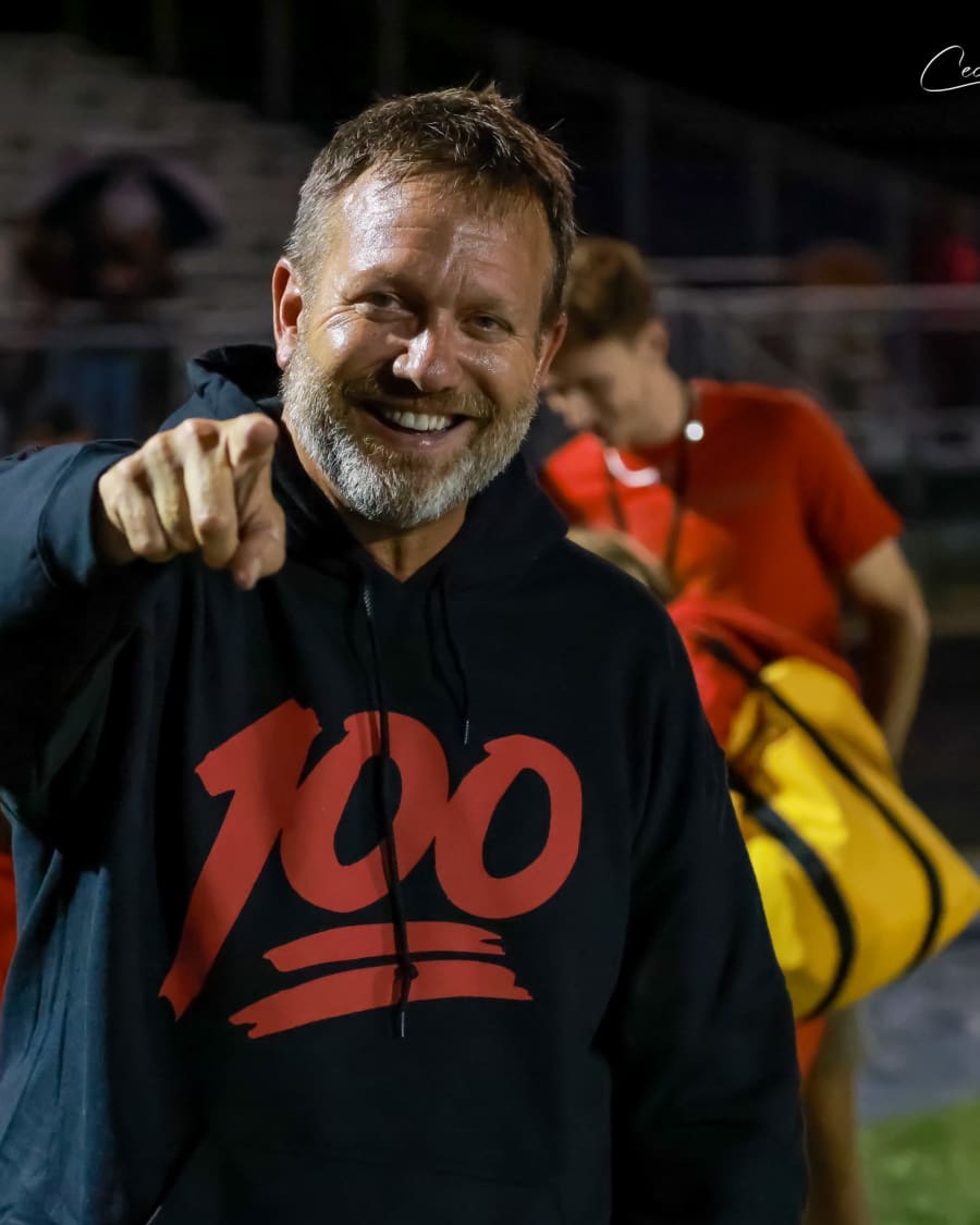 Coach Dennis Piron grinning and pointing at the camera on the Bulldog sideline