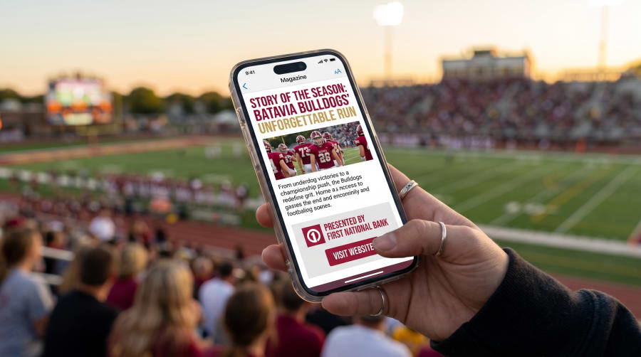 Fan holding a phone showing the Story of the Season magazine with a sponsor ad and Visit Website button
