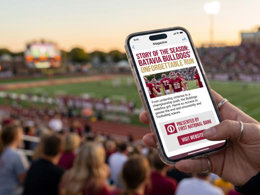 Fan holding a phone showing a sponsor ad with a Visit Website button