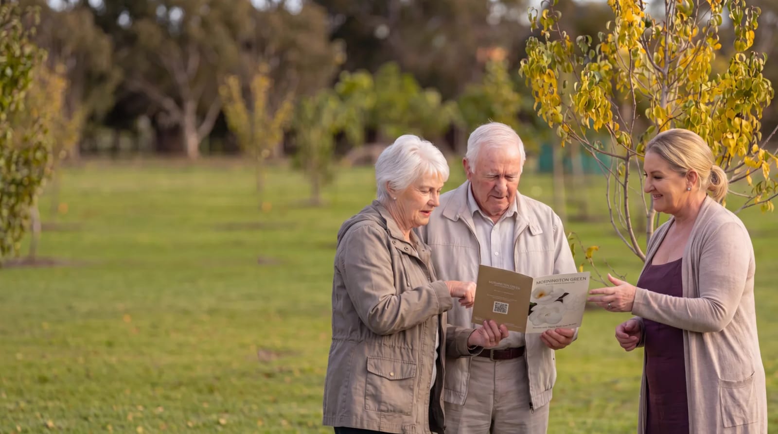 An older couple reviewing a Mornington Green brochure with a memorial consultant among the trees.