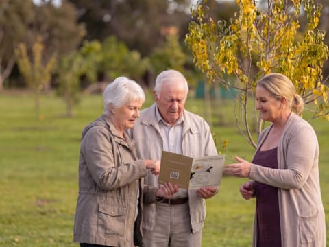 An older couple reviewing a Mornington Green brochure with a memorial consultant among the trees.