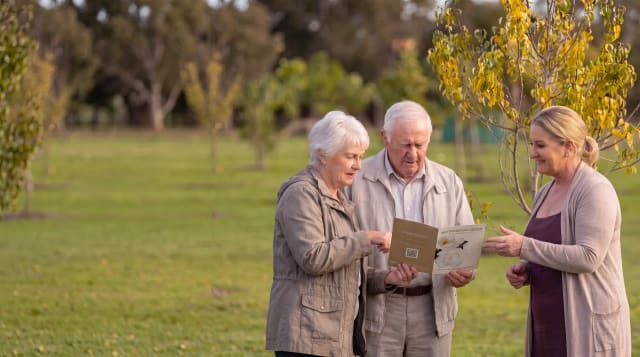 An older couple reviewing a Mornington Green brochure with a memorial consultant among the trees.