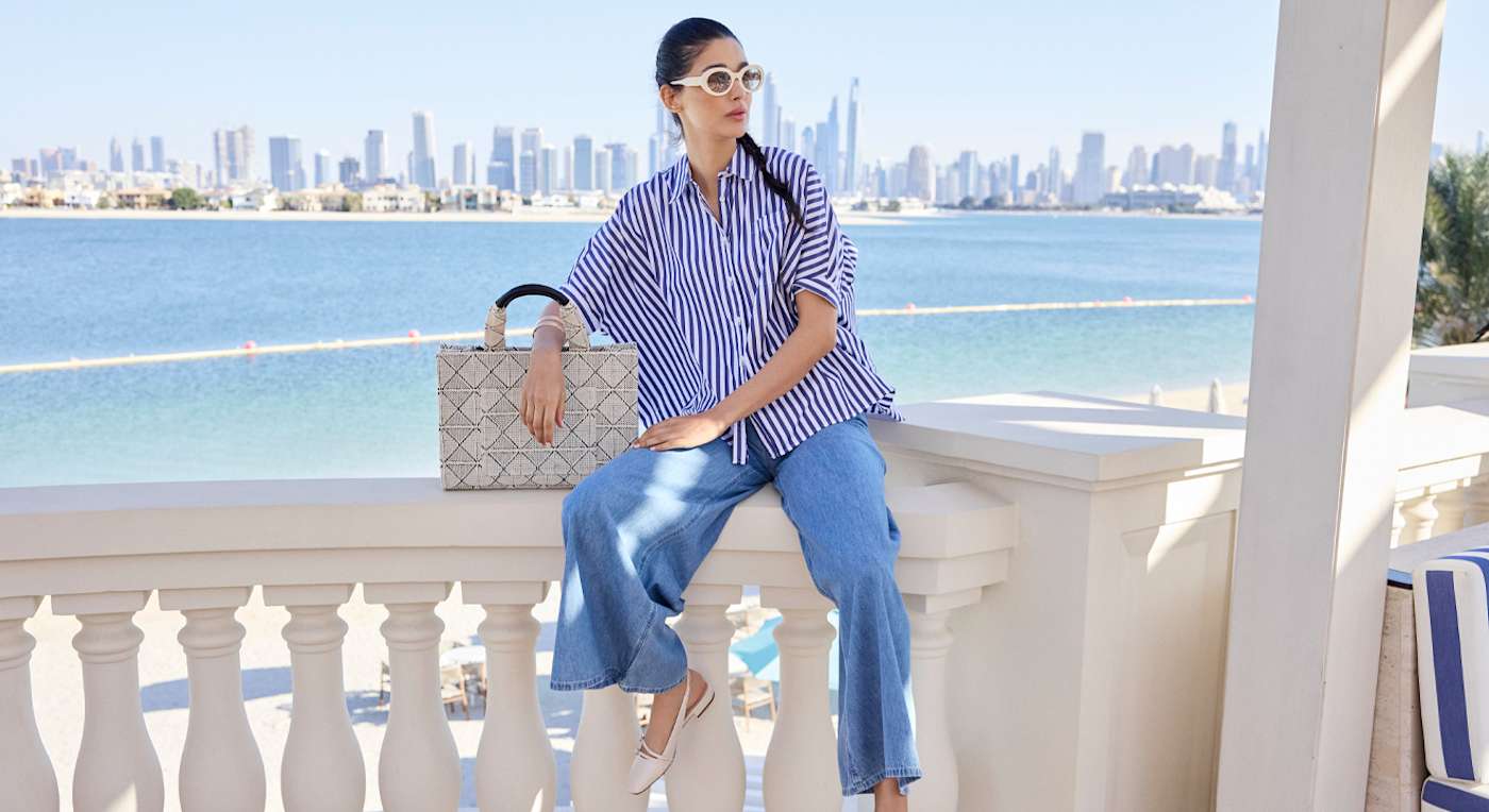 Frau in Marine-Look an Strandpromenade, sitzend auf Steingeländer, mit blau-gestreiftem Top
