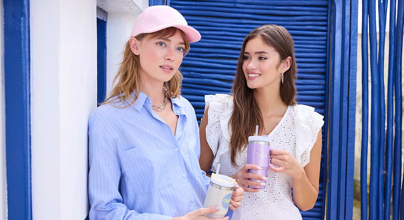 Zwei Frauen in luftigen Sommer-Outfits stehen mit Getränken nebeneinander