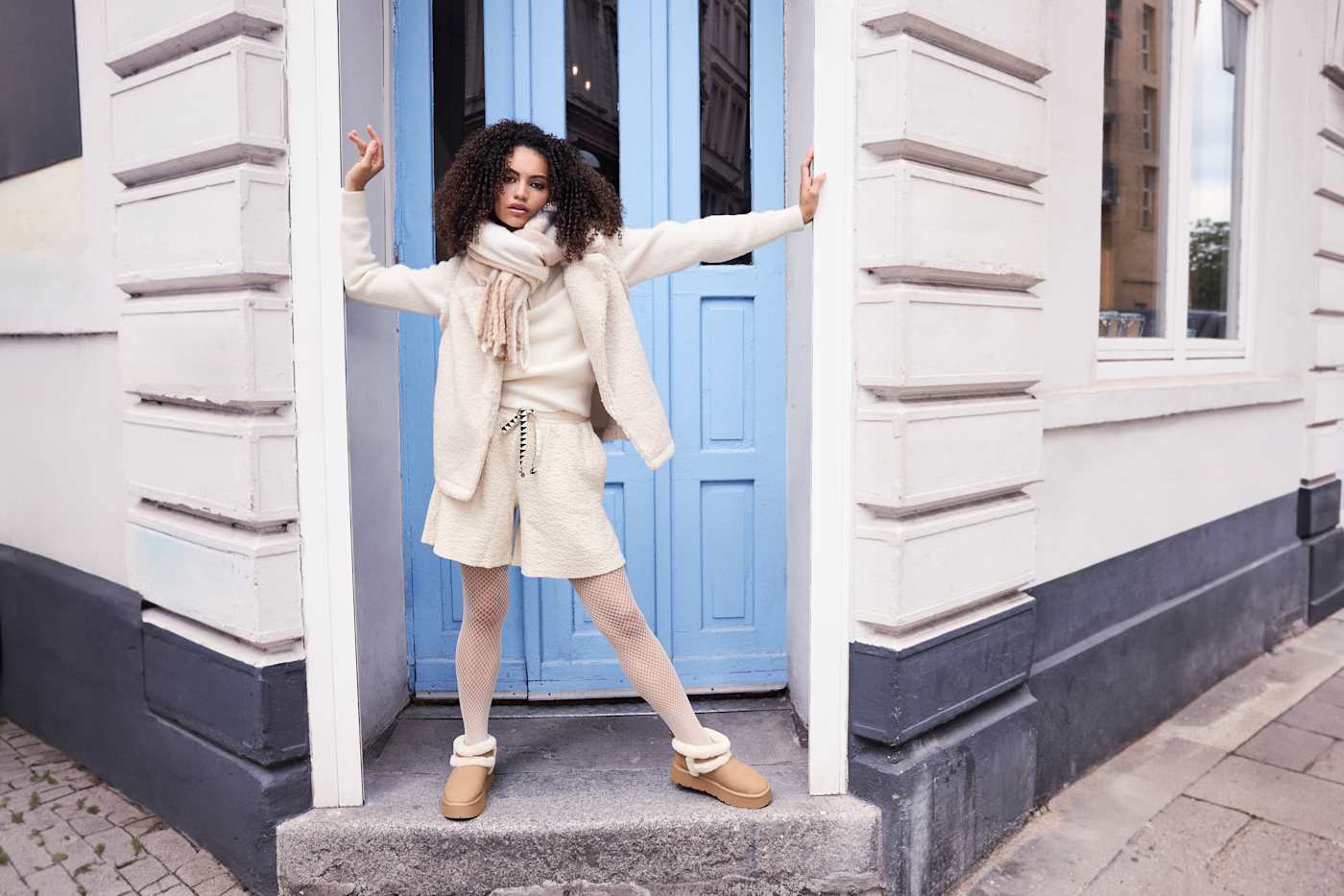 Frau mit weißem Kunstfell-Outfit steht in steinernem Türrahmen