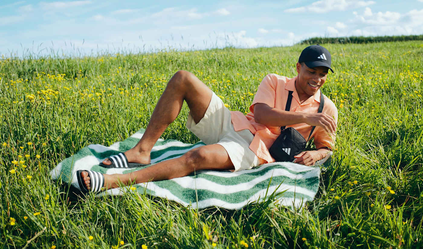 Un uomo con delle infradito Adidas, sdraiato su un asciugamano su un prato verde