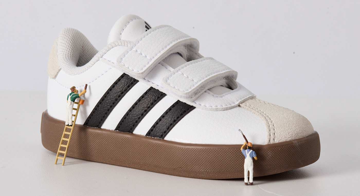 Weißer Sneaker mit schwarzen Streifen und mit Miniatur-Figuren, die ihn reinigen