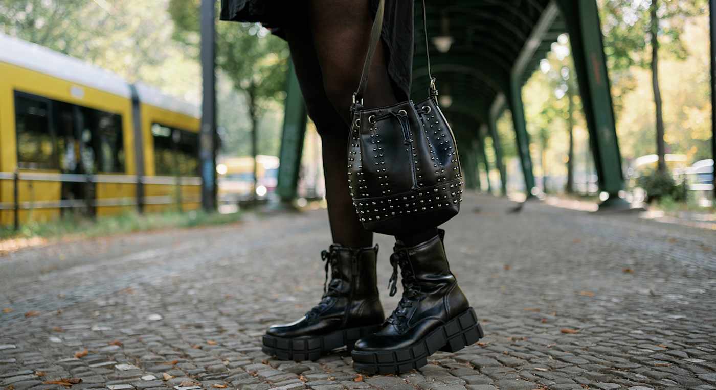 Person mit schwarzen Plateau-Schnürstiefeln und Nieten-Tasche, stehend auf gepflastertem Untergrund