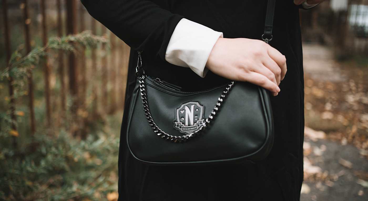 Person trägt eine elegante, schwarze Handtasche mit silbernen Kettendetails und einem wappenförmigen Logo mit dem Buchstaben "N"