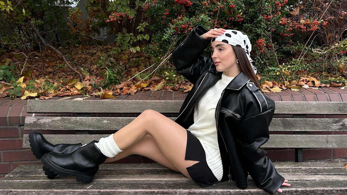 Frau mit schwarzer Jacke, weißem Shirt und Umschlag-Boots, sitzt auf Holzbank