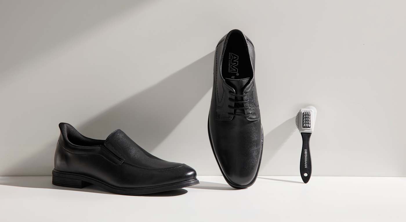 Schwarze Lederschuhe stehen neben einer Lederbürste zum Reinigen