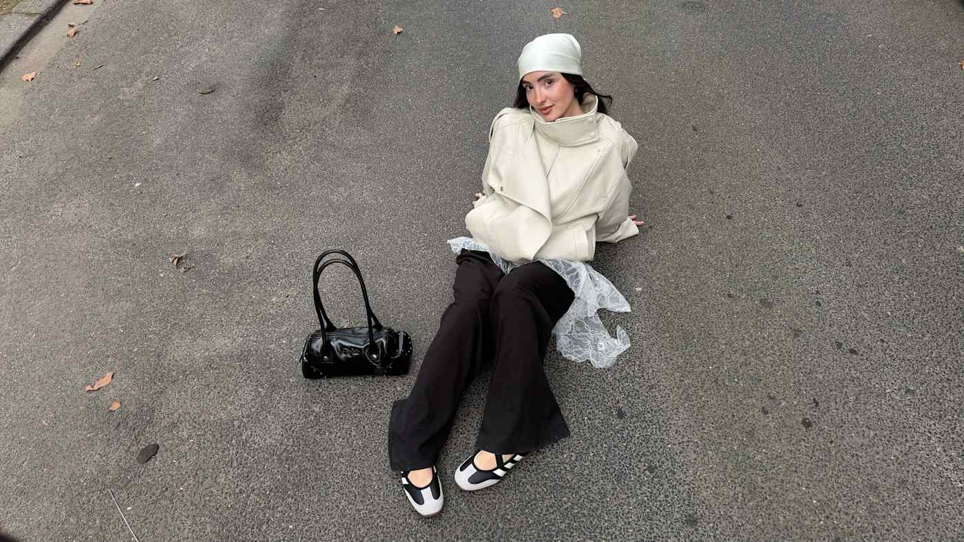 Frau in cremefarbener Oversize-Lederjacke und weiter schwarzer Hose. Im Fokus: Schwarz-weiße Riemchen-Ballerinas im sportlichen Look.