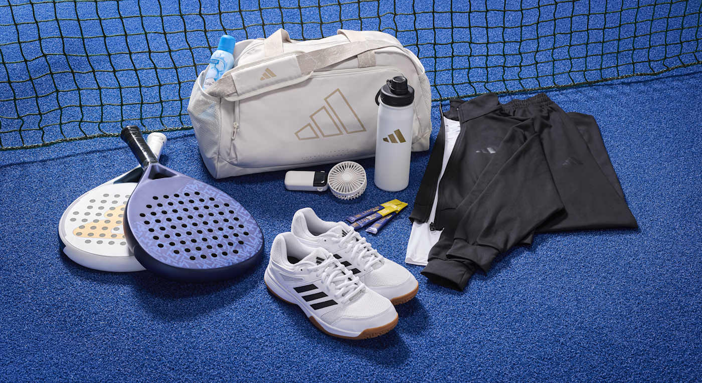 Padel-Schläger, eine Sporttasche, Sportschuhe, eine Trinkflasche und Sportklamotten stehen auf einem blauen Untergrund