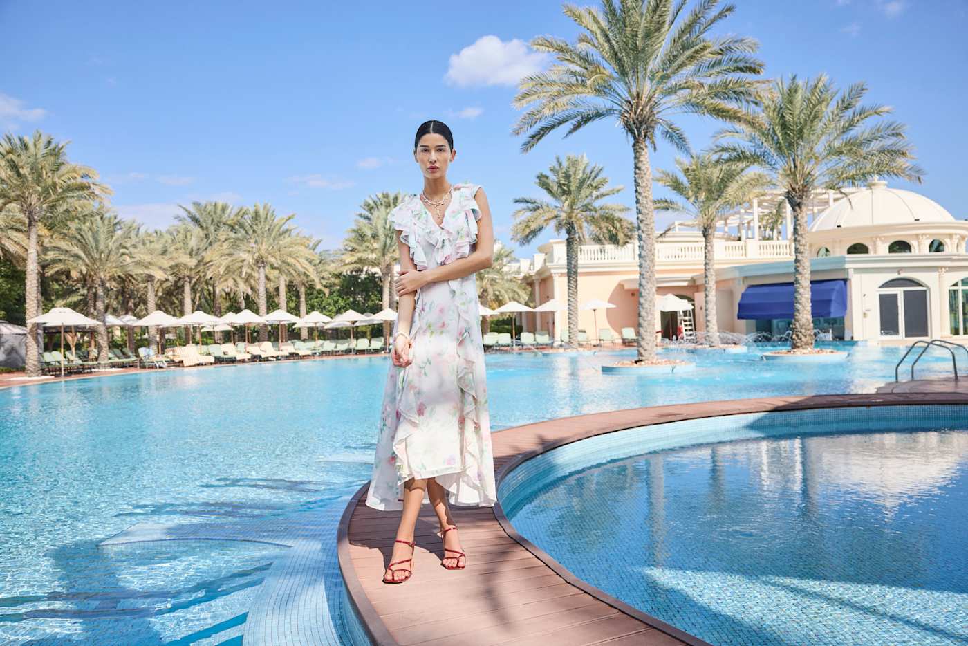 Frau in Floral Outfit, gekleidet in Sommerkleid mit Blumenmotiven, an einem Pool stehend