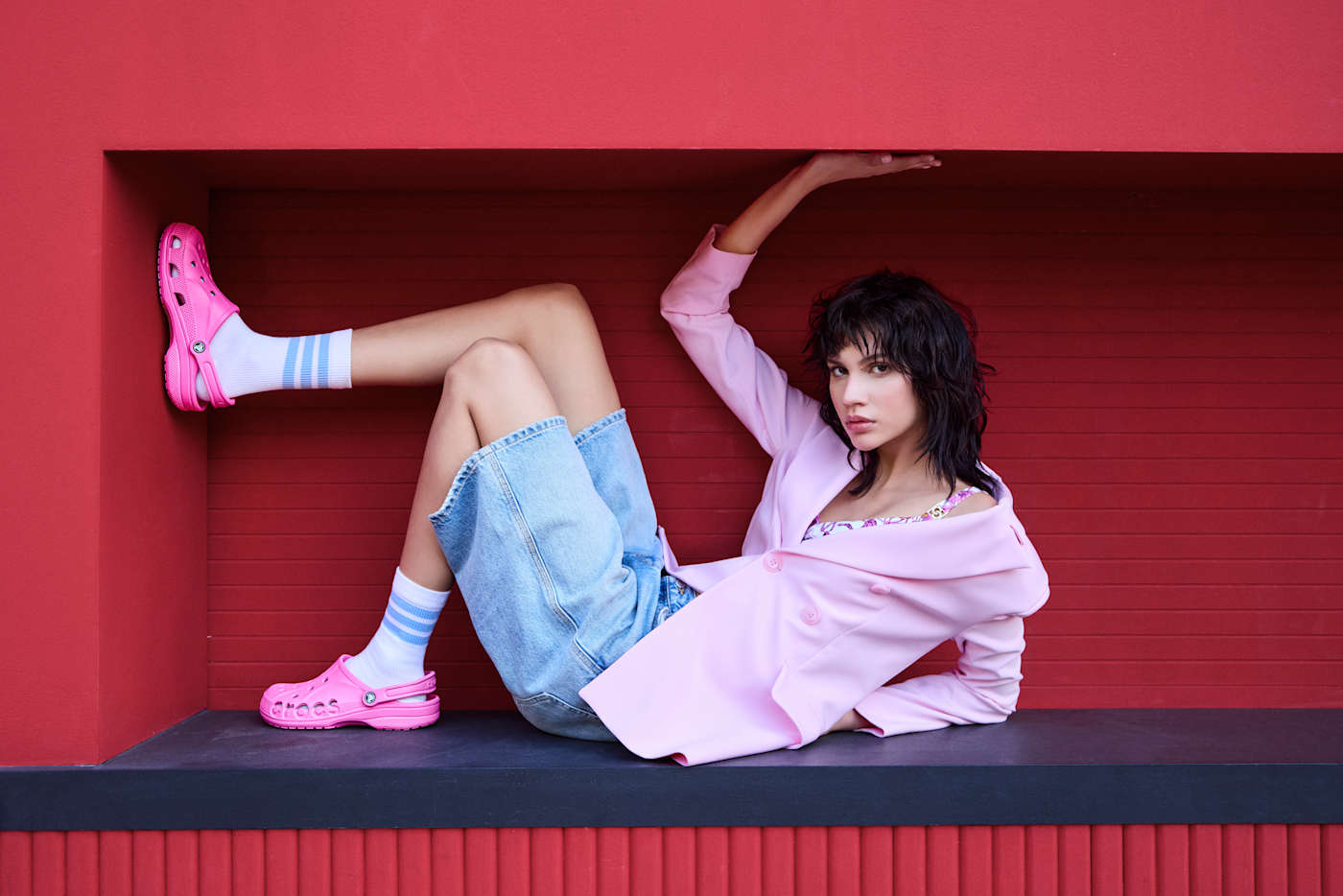 Frau in halbliegender Position, in lockerem Outfit, mit markant-pinken Crocs