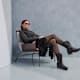 Frau mit Sonnenbrille und Western Boots sitzt in einem Sessel vor grauer Wand