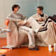 Zwei Frauen sitzen auf einer gemütlichen Couch und tragen bequeme Loungewear in Naturtönen