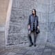 Frau in grauem Mantel und Kleid vor Steinwand kombiniert schwarze Kniestiefel mit Blockabsatz und Minitasche