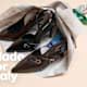 Décolleté slingback in vernice nera e marrone con cinturino a fibbia dorata, adagiate su fogli di giornale italiano