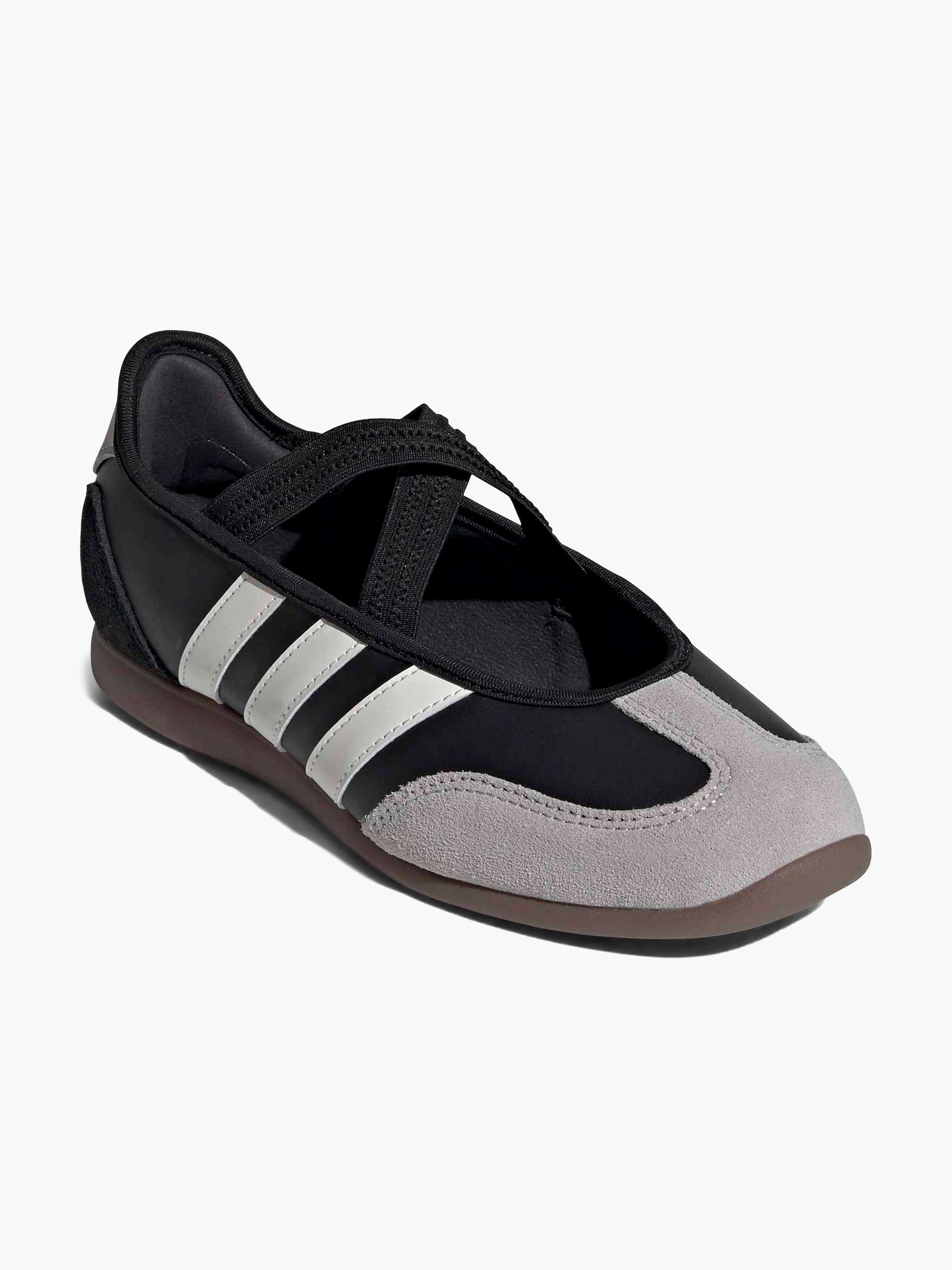 Schwarzer Sport-Ballerina mit grauen Wildleder-Einsätzen, weißen Kontraststreifen, elastischen Überkreuz-Riemen und flacher, brauner Gummisohle.