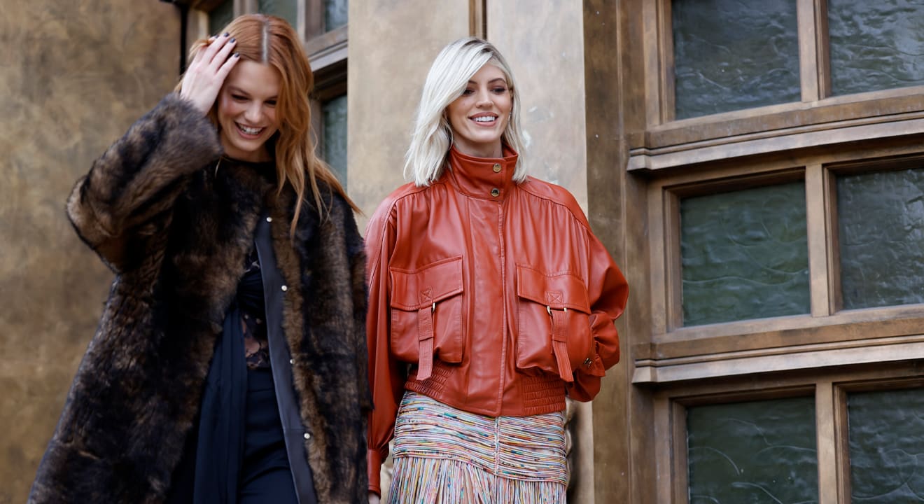Zwei Frauen stehen nebeneinander, beide in unterschiedliche Outfits gekleldet - eines gedeckt, das andere mit knallroter Jacke
