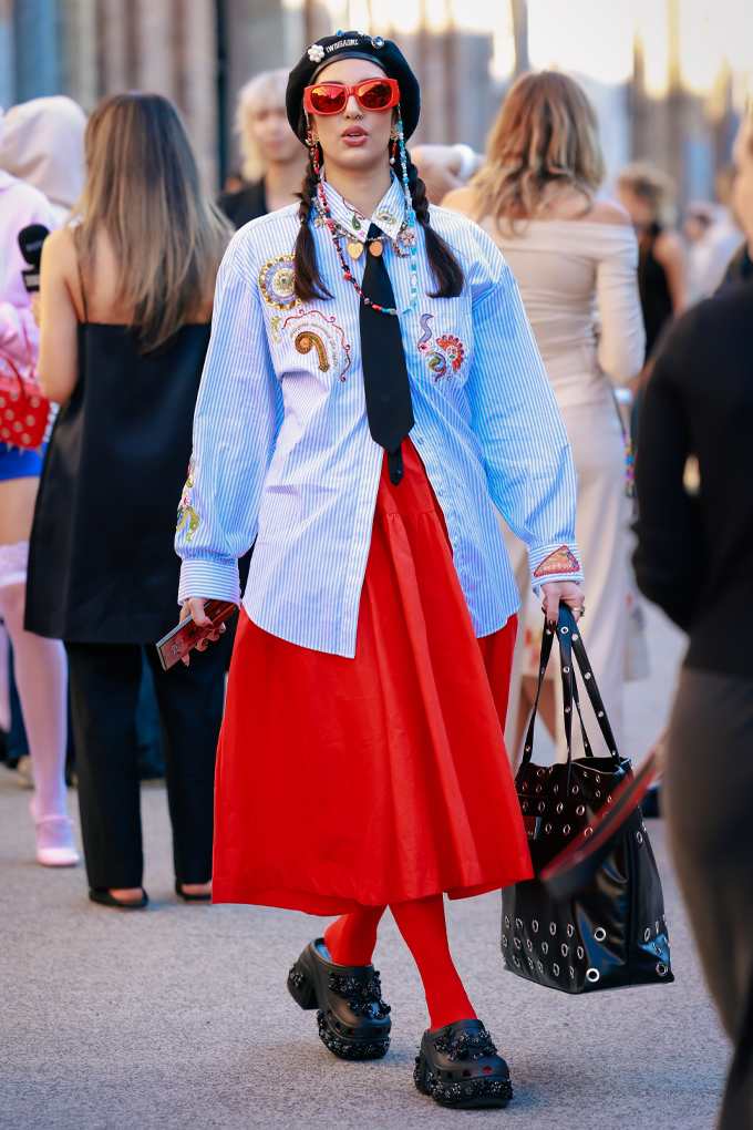 Frau mit Zöpfen in buntem Outfit mit blauer Jeansjacke, kontrastierendem roten Rock und schwarzen Crocs