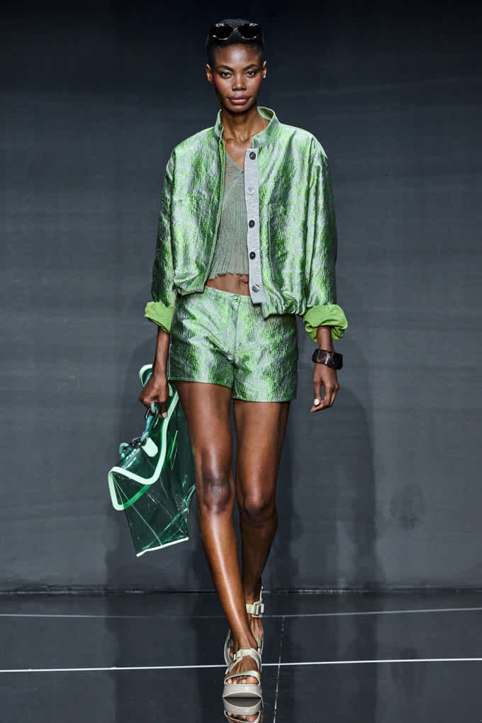 Frau in Outfit in grünem Metallic-Look, kombiniert mit passender Handtasche und schlichten Sandalen