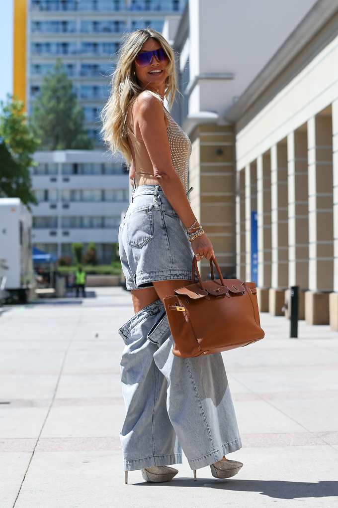 Blonde Frau steht lächelnd in urbaner Umgebung, trägt Jeans-Hose mit massiven Cut-Outs