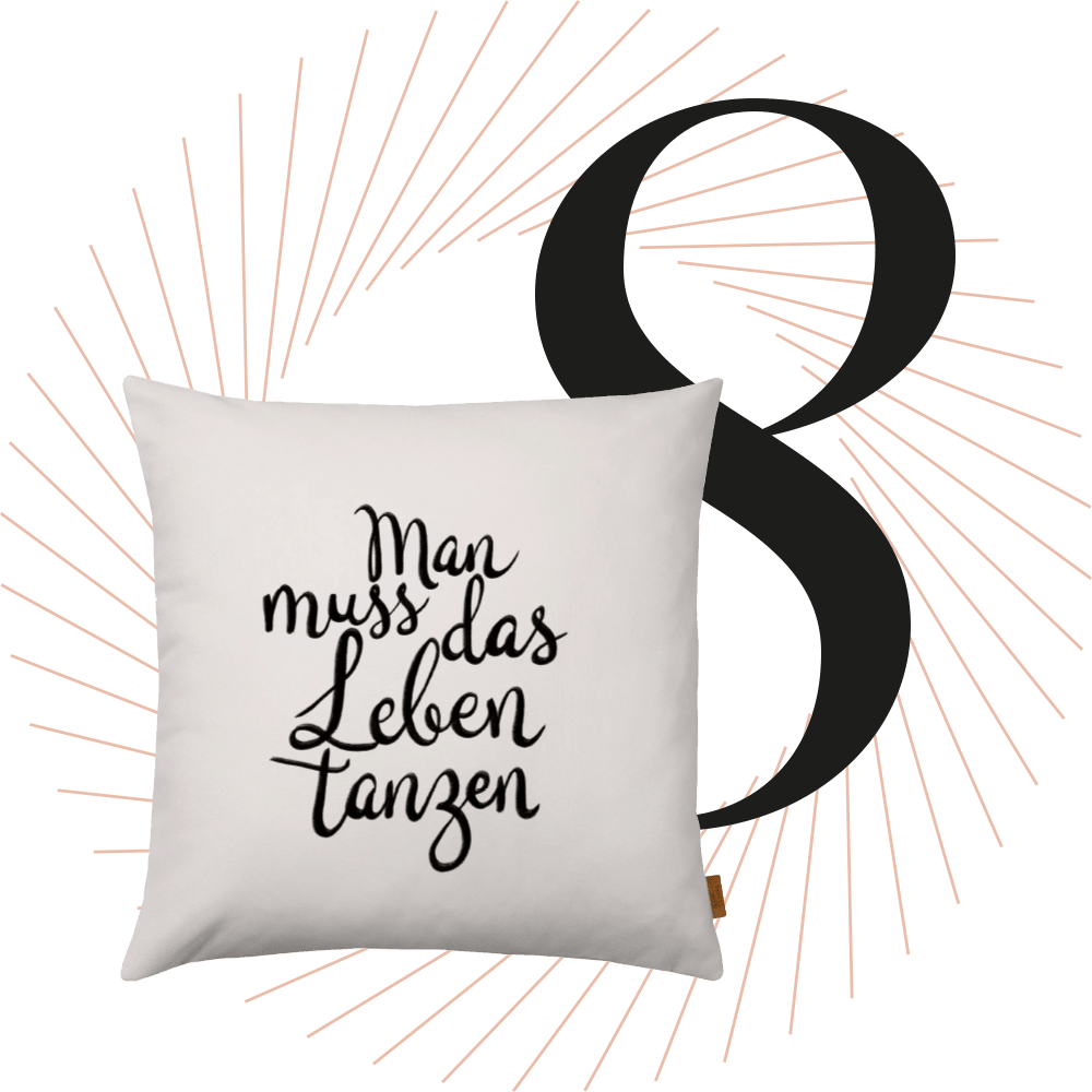 Weißes Kissen mit Aufschrift "Man muss das Leben tanzen", schwarze Ziffer 8 im Hintergrund