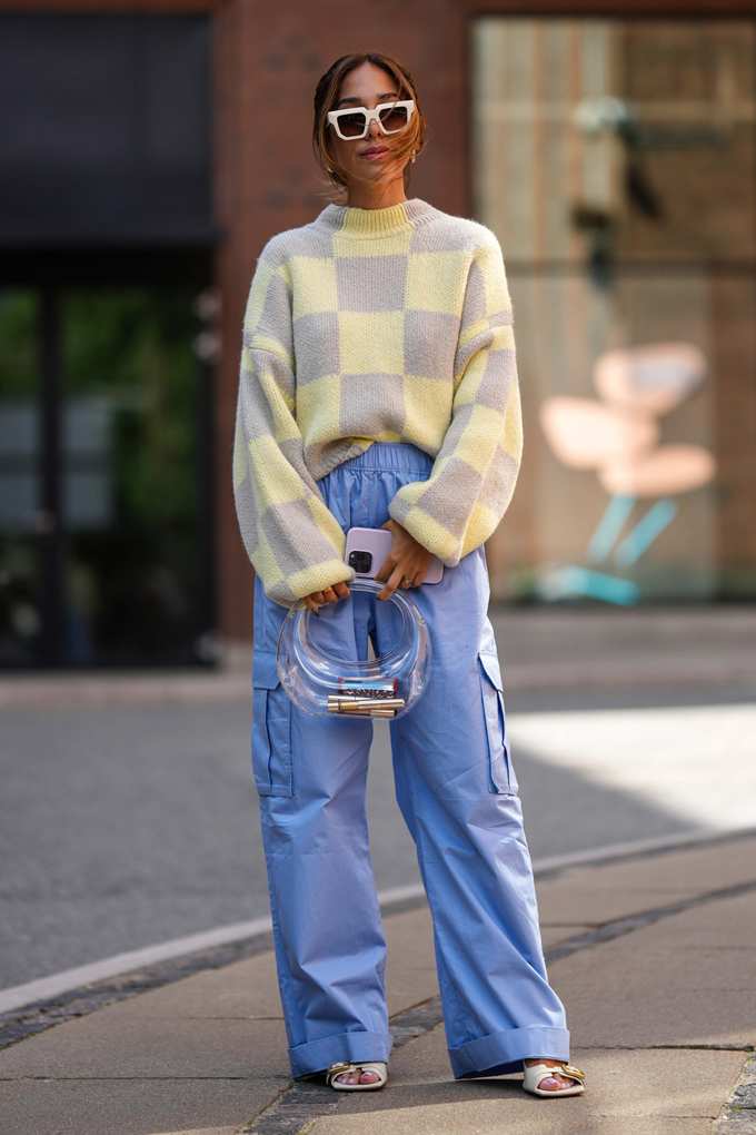 Kariertes Strick-Sweater halb in weite, hellblaue Hose gesteckt – kombiniert mit runder Tasche und Statement-Sonnenbrille
