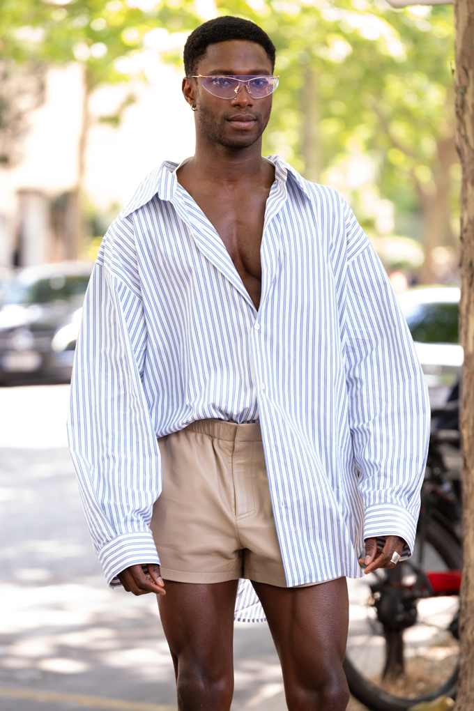 Mann trägt blau-weiß gestreiftes Oversize-Hemd im French Tuck zu beigen Shorts, ein lässiger Sommer-Look mit Fashion-Statement