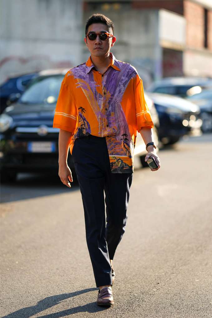 Mann trägt ein Outfit mit einem Statement-Hemd im knalligen Sunset-Print, lässig im French Tuck zur Anzughose