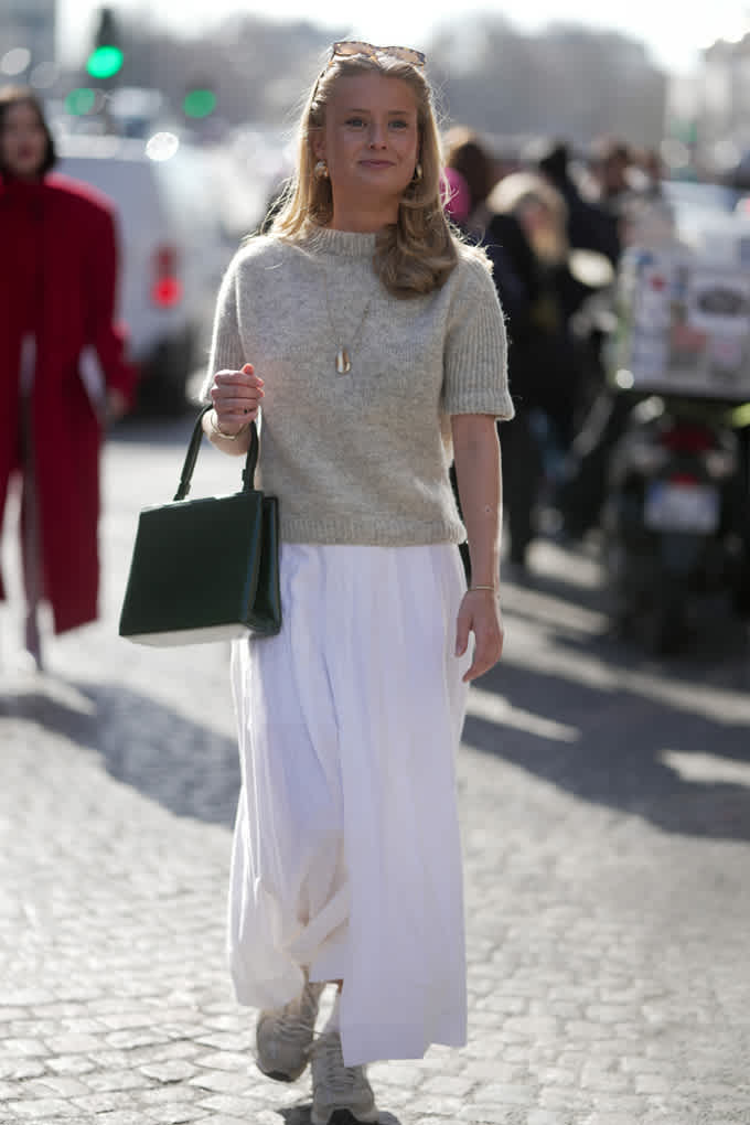 Frau in minimalistischem Strick-Outfit, hellgrauer Pullover mit bodenlangem weißen Rock