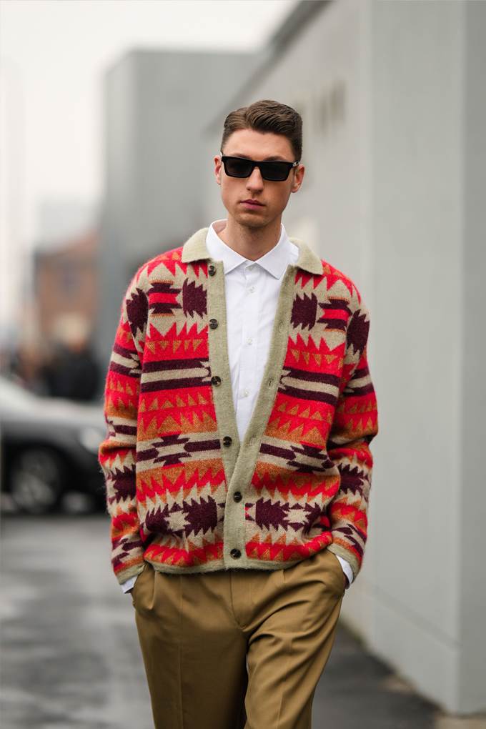 Mann trägt schwarze Sonnenbrille und rot-braunen Ikat-Cardigan mit brauner Hose