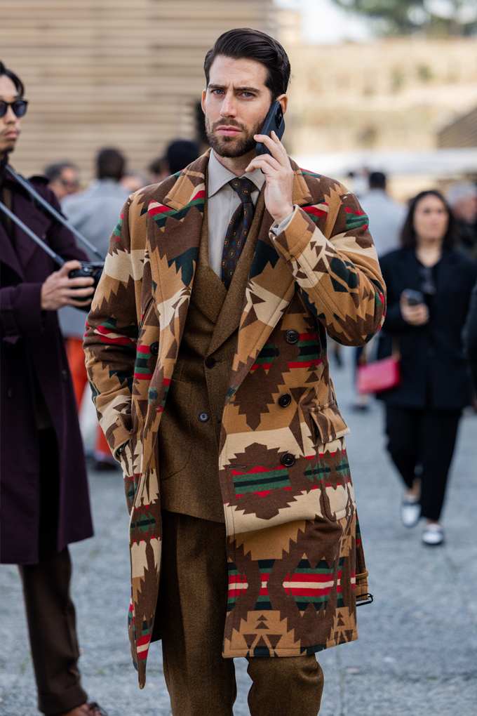 Mann in Business-Look, trägt braunen Mantel im Ikat-Design über Anzugkombi